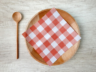 Top view of Empty wooden plate with red white checkered paper napkin and wooden spoon on a wooden table. Dining set background concept for food poster mock up. Simple table setting with wood theme.
