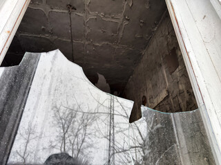 Broken window reveals abandoned interior with peeling paint and visible debris outside