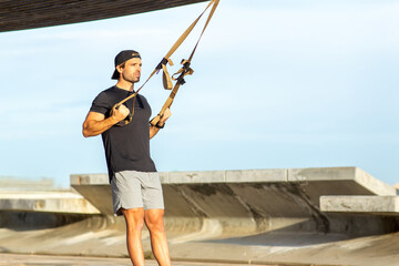 Man in athletic outfit performing resistance training with suspension straps outdoors