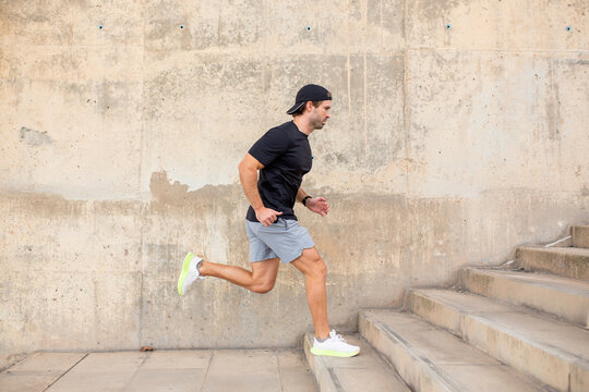 Man in sportswear running up stairs alongside a concrete wall during fitness session