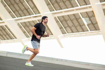 Man in sportswear sprinting outdoors near a modern structure during fitness training