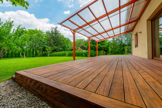 Wooden garden deck with a polycarbonate pergola roof, surrounded by a lush green backyard and landscaping, providing a shaded outdoor relaxation area