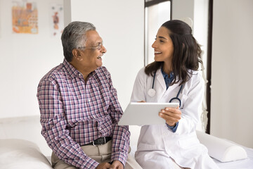 Patient care and digital technology. Happy laughing young woman doctor old age retired man patient having fun looking on tablet computer screen excited with good examination results health improvement