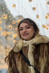 Smiling woman in a cozy fur coat against a backdrop of sparkling lights during a winter evening...