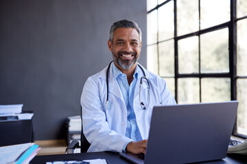 Portrait of middle eastern doctor using laptop while smiling at camera