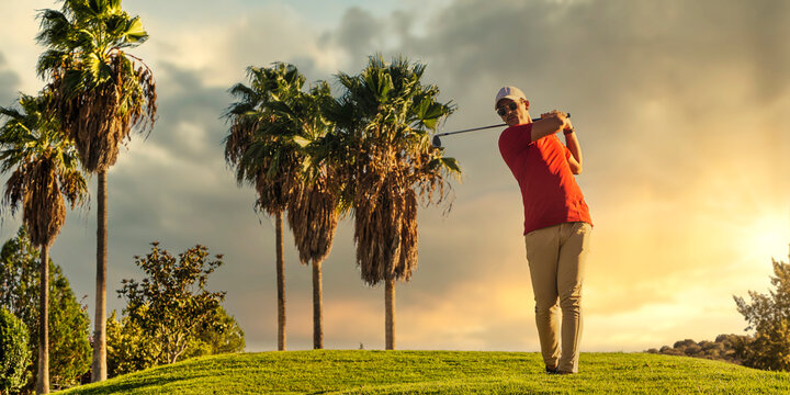 Golfer hitting a golf ball on a lush course with palm trees during a golden sunset