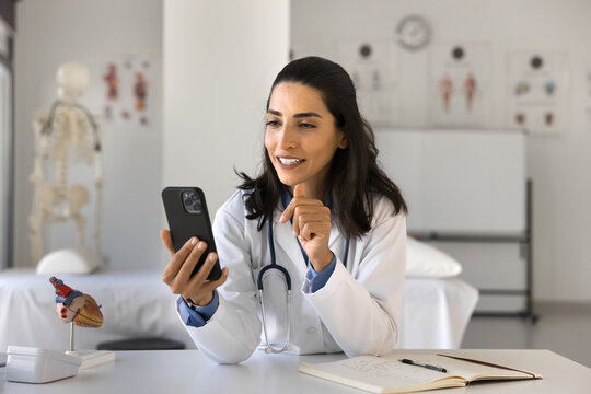 Mobile medical software. Happy woman doctor use telehealth app on phone at workplace manage electronic prescription communicate with healthcare team text message to patient calculate medication dosage - Powered by Adobe