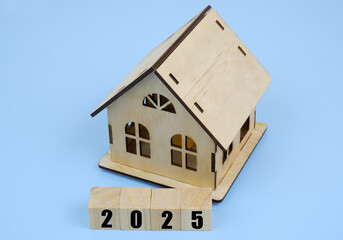 Wooden house and wooden cubes with numbers 2025 on blue background. Real estate market in 2025.