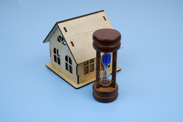  Wooden house model and hourglass on blue background.