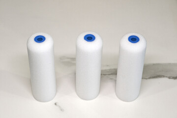 White foam paint roller refills with blue plastic cores, standing upright on a neutral background. Ideal for smooth surface painting.