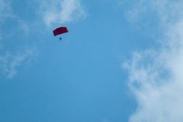 Skydiver parachutist with open parachute flying in bright blue sky