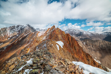 Vivid sharp pinnacle in sunlight. Shiny pointy peak of gold color. Colorful red rocky peaked top. Freshly fallen snow in high mountains. Sunny cloudy alpine view. Snowy cornice on stony mountain ridge