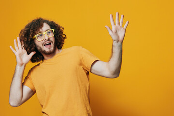 Cheerful young man with curly hair in yellow glasses expressing joy against a bright yellow...