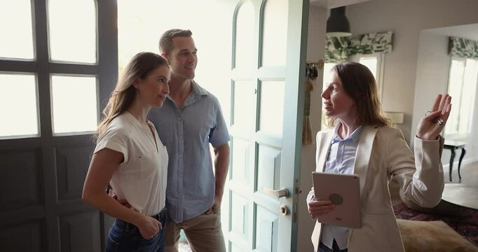Professional realtor woman talking to new tenants, meeting with couple of renters in accommodation for rent, telling about apartment, holding digital tablet, showing house for sale, giving tour
