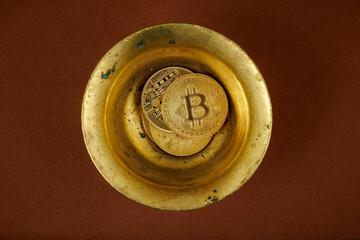 Golden bitcoins inside an antique container on a brown background.