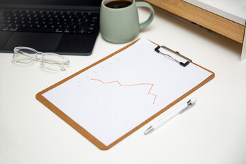 Office workplace table with charts report on wooden clipboard, coffee, supplies and laptop.