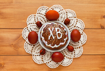 Easter composition with homemade tradition Easter cake on lace handmade napkin and painted red Easter eggs on wooden table. On Easter cake russian letters ХВ mean Christ is Risen. Flat lay, close-up