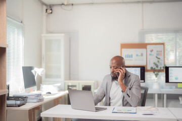 Focused African American businessman multitasking with a laptop and phone call, showcasing...
