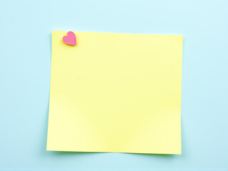 Naklejka premium Blank yellow sticky note with pink heart on blue background ready for messages or reminders