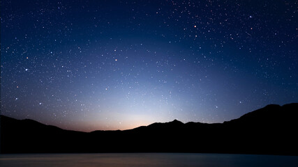 A movement of stars in the night sky with the view of mountains..