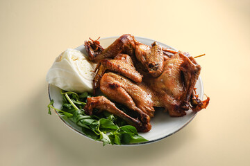 whole Ayam Penyet with sambal, basil and cucumber served in brown paper, showcasing Indonesian cuisine