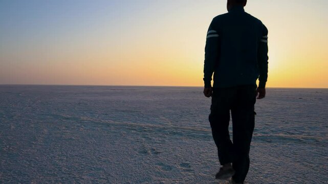 young man paying salutation to holy sun at white desert with sunset orange dramatic sky at dawn