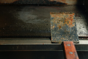 A dirty stainless steel spatula resting on a flat griddle, dirty kitchen concept
