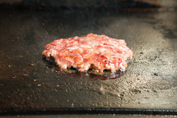 A beef patty is cooked by pressing it onto a hot flat griddle