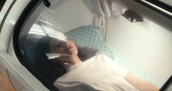 A young woman lying inside a hyperbaric oxygen chamber, seen through the glass. Represents medical treatment, wellness therapy, and advanced healthcare technology