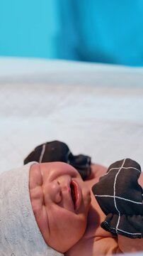 Just born infant crying bitterly on the table. Newborn baby is dressed in a cap, mittens, socks and diaper. Vertical video
