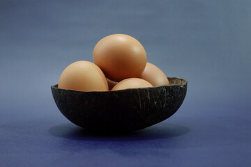 Fresh Brown Eggs in a Natural Coconut Shell Bowl on Blue Background