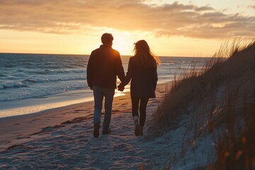 A young couple holding hands while walking along the shore at sunset.