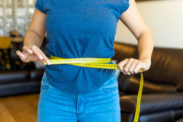 Woman measuring her waist with yellow measuring tape at home