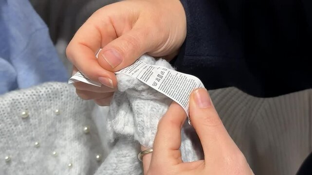 A Caucasian person checks a care label on a wool sweater, emphasizing winter fashion and sustainability