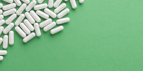 Scattered white medicine, pills or capsules on green table. Mock up background from top view with a copy space. Medical, pharmacy and healthcare. High-quality photo mock-up banner