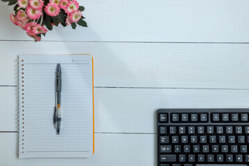 Computer keyboard, notebook and flowers on white table
