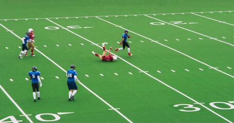 American Football Clash Unfolds as Professional Male Athletes Tackle Competition on a Green Outdoors Field. Agile Blue Footballer Running Away with the Ball From a Fallen Competitor