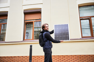 Man holding photovoltaic solar panel in front of historical building. Concept of integration of...