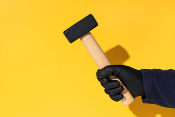 Construction worker holding a mason's hammer isolated on yellow background with copy space