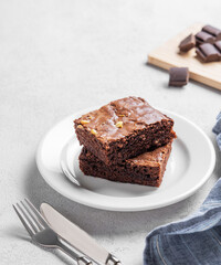 Chocolate brownie with nuts cut into pieces on a plate on a light background with fork and napkin.