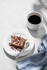 Pieces of chocolate brownie with nuts on a plate with a cup of espresso coffee on a light background