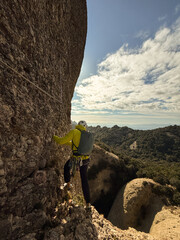 A man in a yellow jacket is climbing a rock wall
