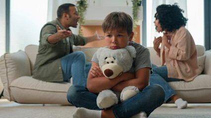 Sad little child boy hug teddy toy while mom dad fighting screaming arguing upset kid son suffer...