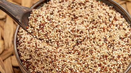Rustic wooden spoon scooping mixed quinoa grains from a bowl. Healthy food concept with organic...