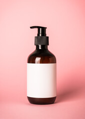 Shampoo bottle with pump at pink background and towels.