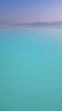 A turquoise tailings pond near a cement factory, surrounded by rugged hills. The vivid water contrasts with the barren land, creating a striking yet industrial scene of environmental impact