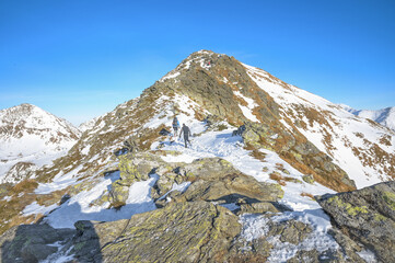 SHikers with backpacks trek along a snowy mountain trail under a brilliant blue sky, showcasing the...