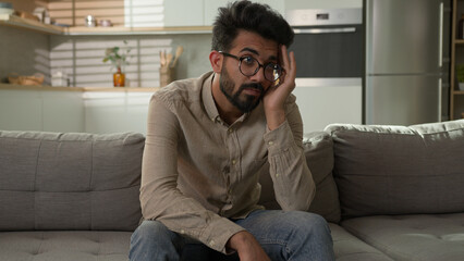 Pensive Indian Arabian man bored on home couch thinking deep in thoughts difficult decision tired...