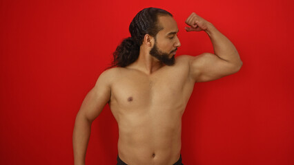 Fototapeta premium Young man with beard poses confidently flexing muscles against vibrant red wall