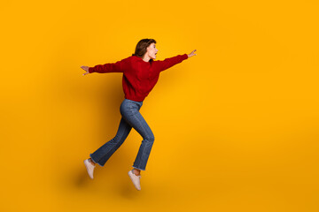 Fototapeta premium Energetic young woman in a red sweater jumping joyfully against a vibrant yellow background
